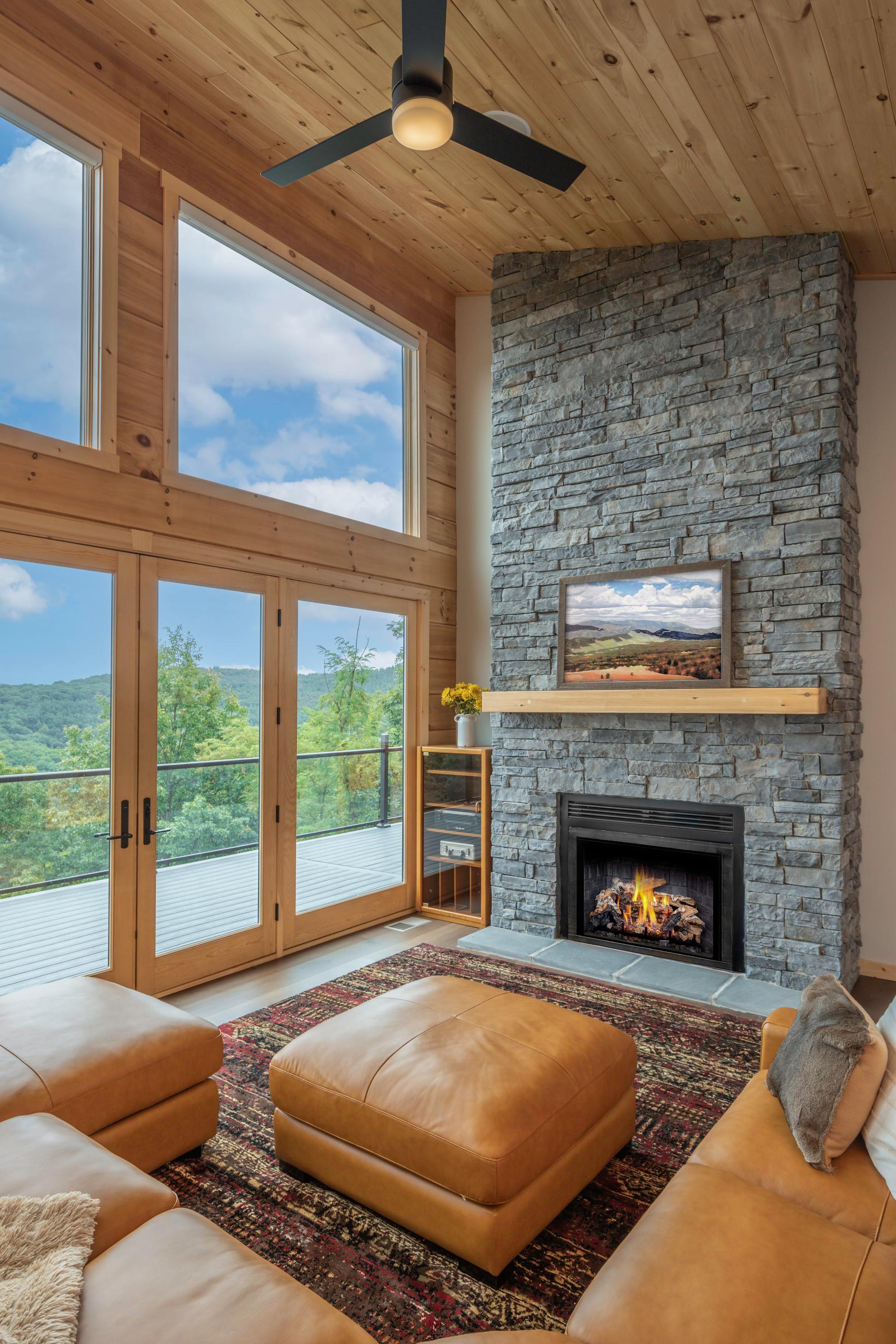 Stacked-stone fireplace with a lit fire and a timber mantel, beside doors onto the deck