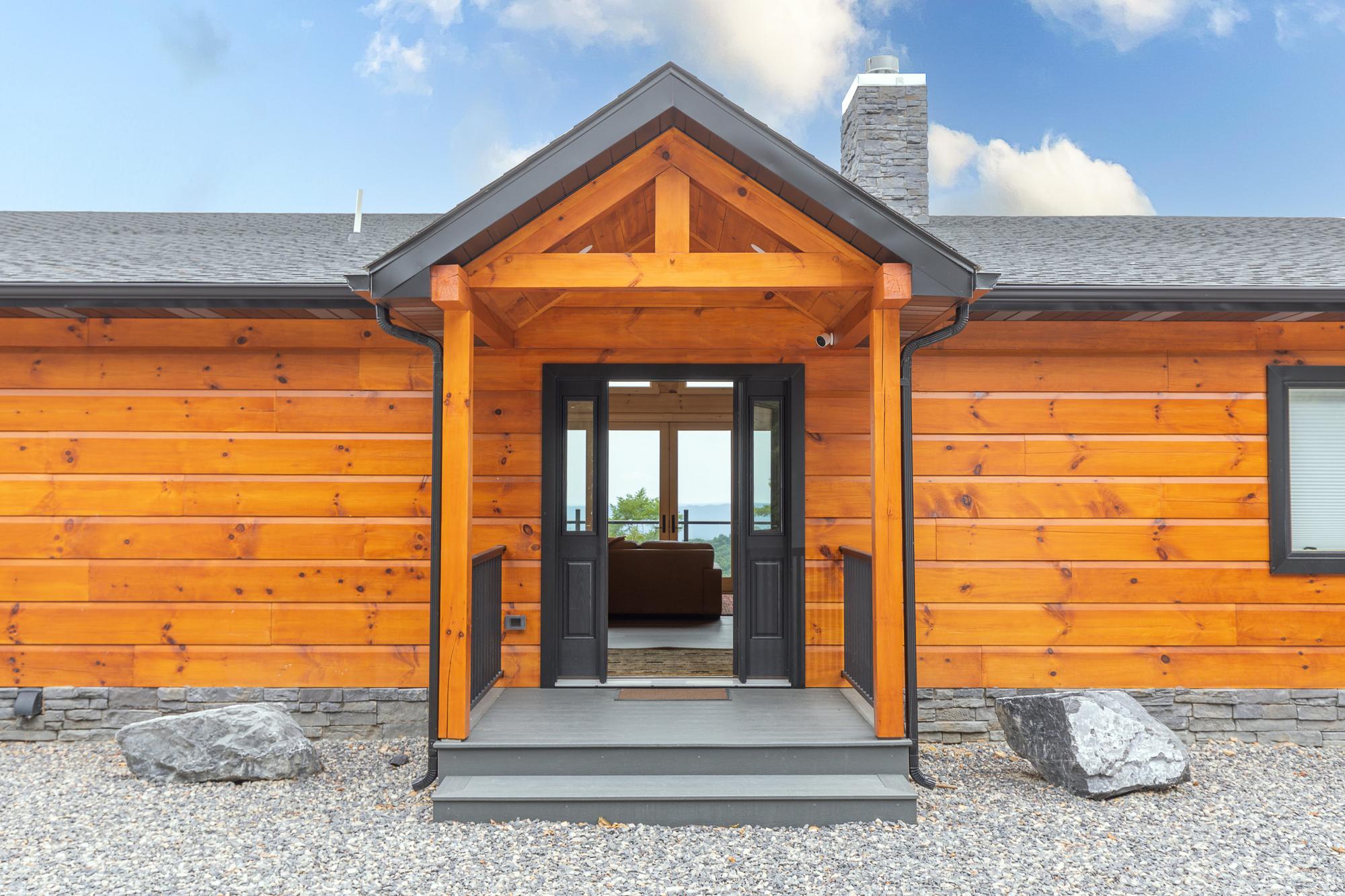 Front entry beneath a timber gable portico, double doors standing open to the valley beyond