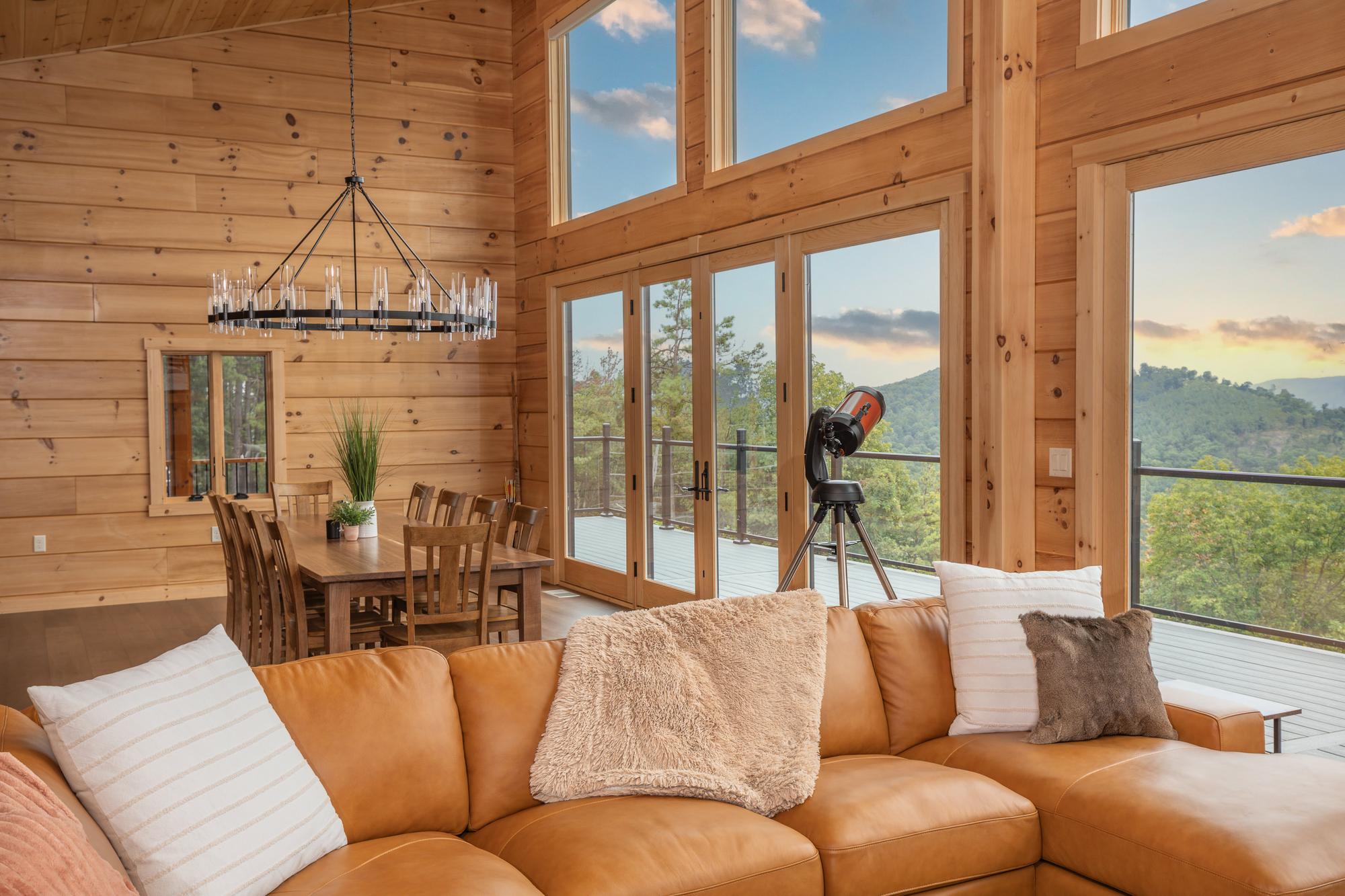 The sectional facing the window wall, with the dining table behind and a telescope beside the deck doors