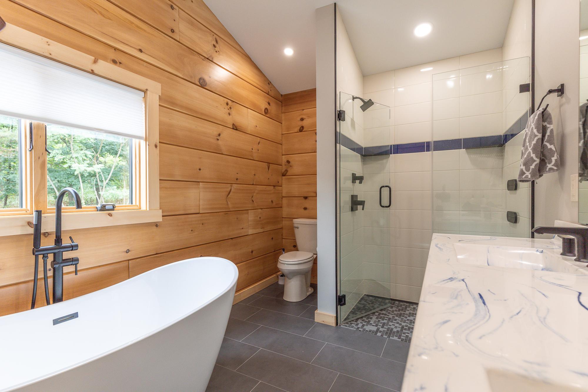Bathroom with a freestanding tub against a wood-paneled wall, a tiled shower and a marbled vanity top