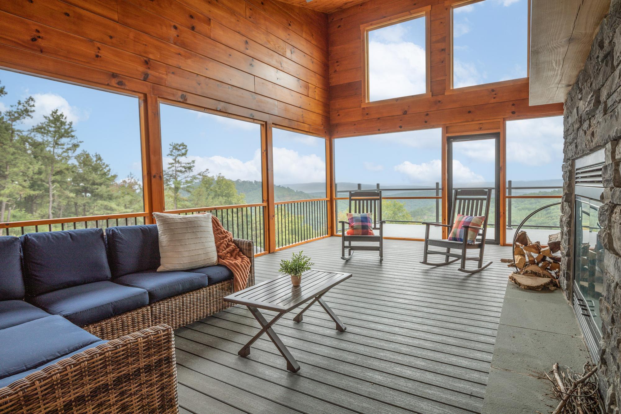 Screened porch with a wicker sectional, two rocking chairs, a stone fireplace and layered ridges beyond