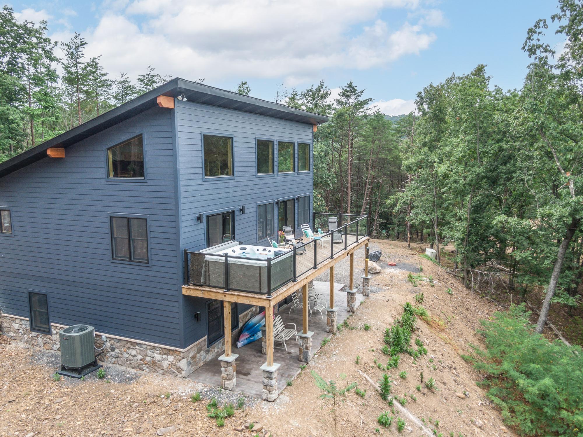 The rear of the home from the air, with its elevated deck, hot tub and glass railing above the treeline