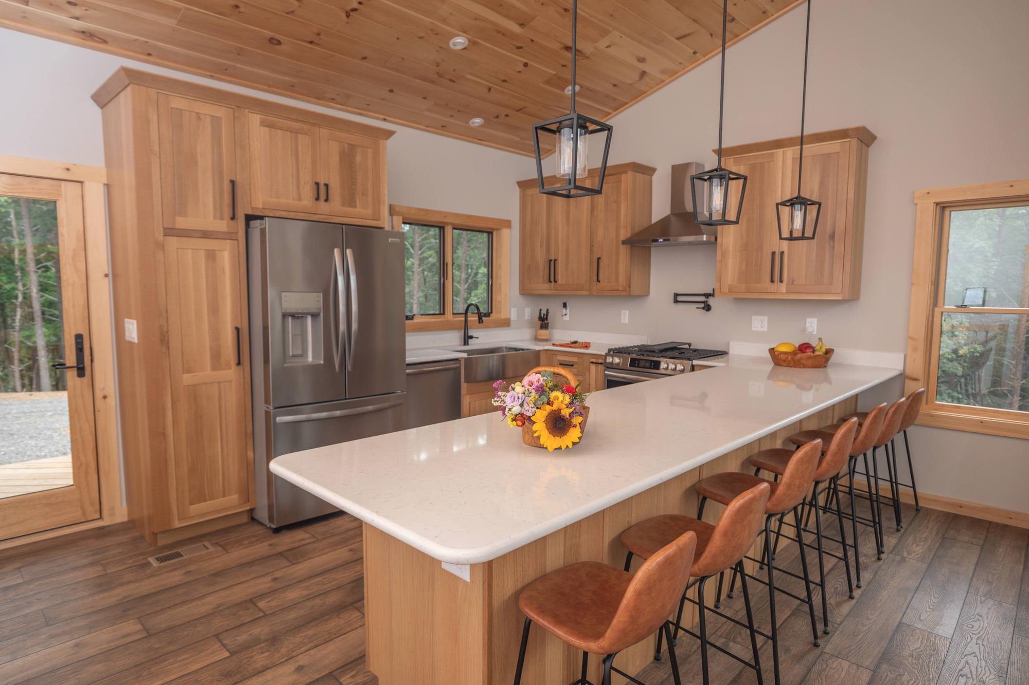 Kitchen with hickory cabinets, a white quartz peninsula, lantern pendants and leather bar stools