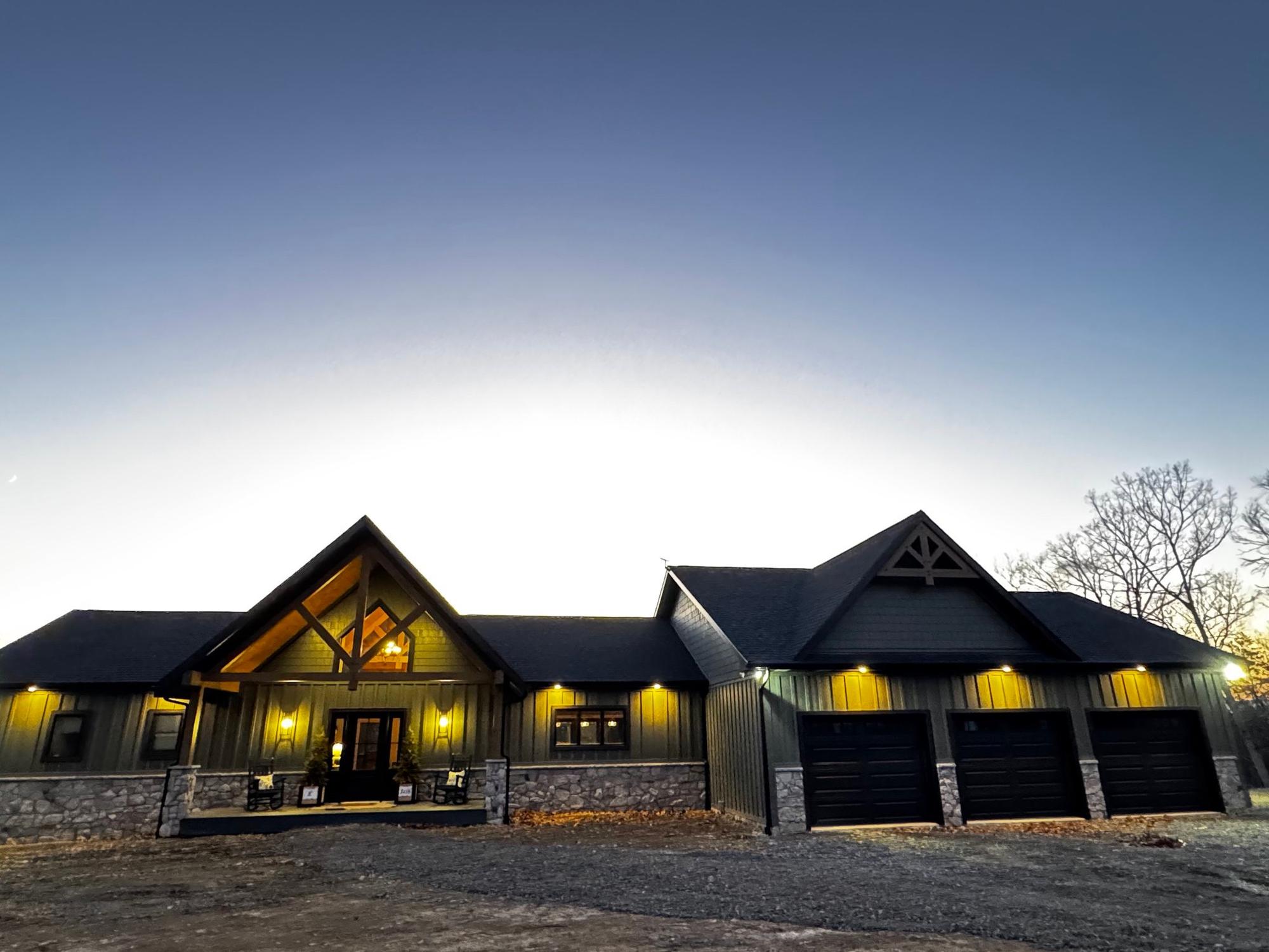 The front elevation at dusk, porch and soffit lights lit and the gable truss glowing above the entry