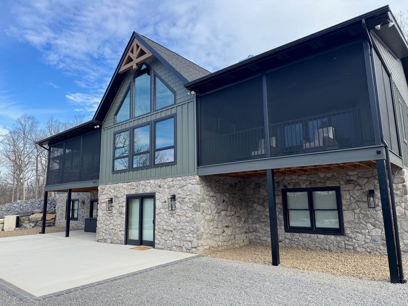 Rear elevation with screened porch either side of a timber-trussed gable window wall, above a stone walkout level