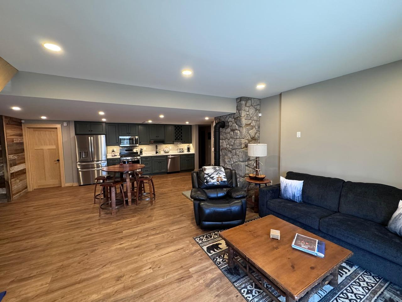 Lower-level family room opening to a kitchenette, with a stone chimney chase between them