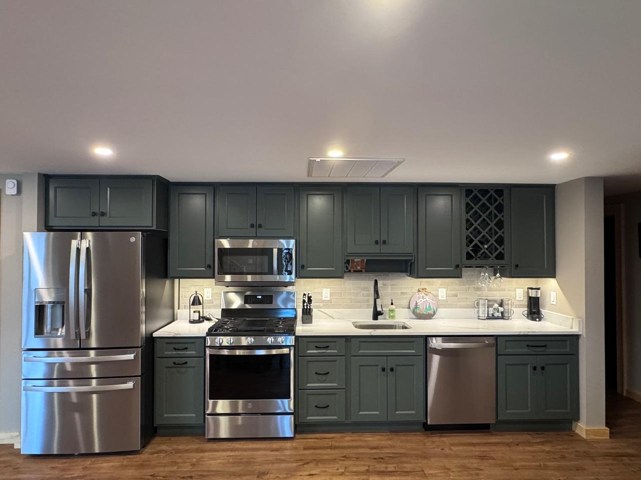 The lower kitchenette in dark green cabinetry, with a wine rack and quartz counters