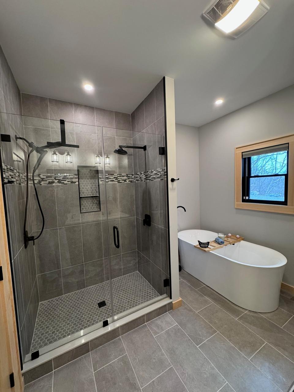 Tiled walk-in shower with a rainhead and a mosaic band, beside a freestanding tub