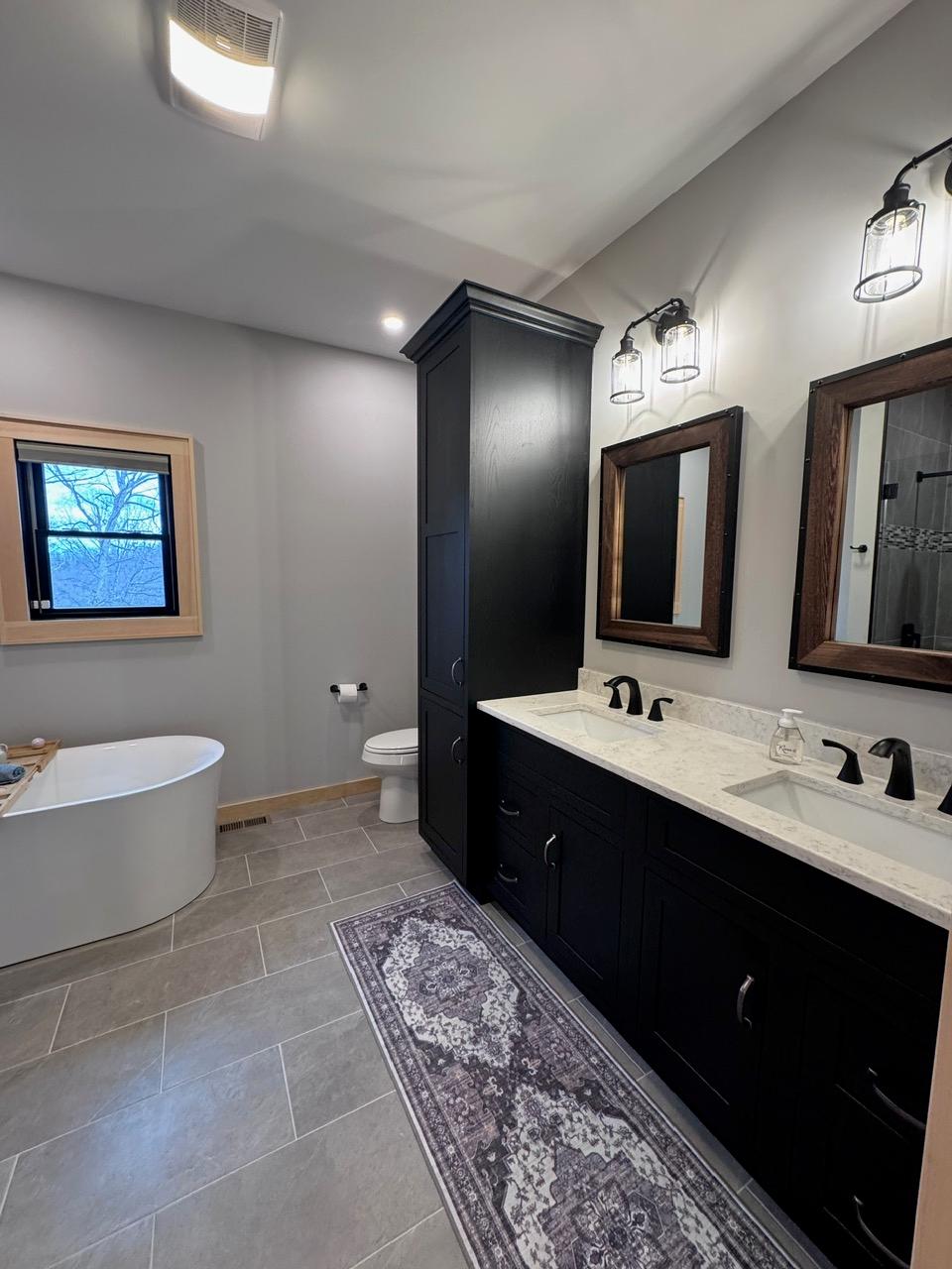 Main bathroom with a black double vanity, wood-framed mirrors and lantern sconces