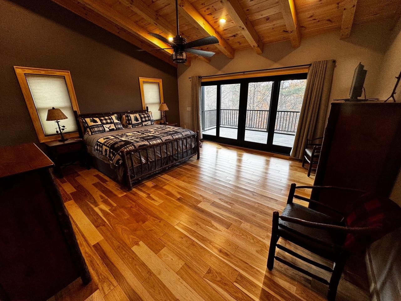 The main bedroom at dusk, bedside lamps lit and the deck doors dark beside the bed
