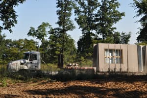A flatbed tractor-trailer parked on the site carrying gray precast concrete wall panels stood on edge, window openings already cast into them.
