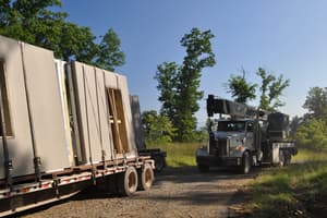 A second trailer of panels waiting behind the first, the load strapped upright, a boom truck at the end of the drive.