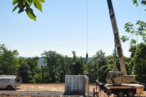 The crane boom raised against the trees, an outrigger set on the bare pad, ready to start setting panels.