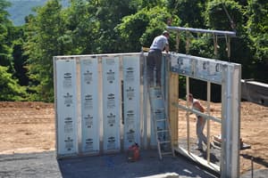 Two of the crew guide a precast wall panel with a door opening into place while the crane holds it on a spreader bar.