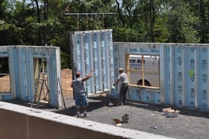 Two of the crew line up a tall precast panel between finished wall sections, a ladder leaning against the wall at left.