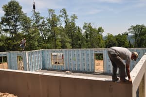 A crew member works along the top of a finished basement wall while the crane sets another panel across the pad.