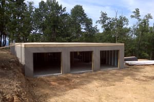 The lower level from the downhill side, three garage openings cast into the wall and the bank cut back behind.