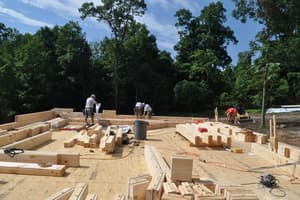 Log courses laid out across the whole subfloor, stacks of cut timber waiting and the crew spread out at the far end.