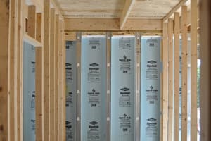 Interior partitions framed on the lower level's concrete floor, stud walls meeting a foundation wall faced in blue rigid insulation.