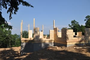 Log walls standing a few courses high on the foundation, with tall corner posts reaching up against a clear sky.