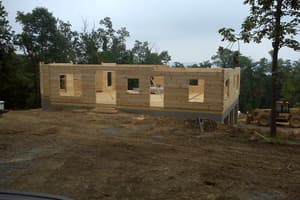 The long elevation from the drive: walls up, openings cut, the whole footprint of the house now standing in log.