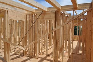 Interior stud walls framed on the main floor with diagonal braces, beams spanning overhead and open sky where the roof will go.