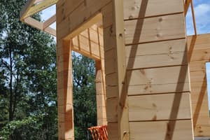 A dormer framed out against the sky, new joists and sheathing pale against the darker log wall below.
