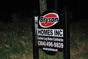 A Bryson Homes Inc sign at the roadside — Custom Log Home Contractor, with the phone number and brysonhomes.net.