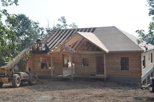 The roof going on, trusses set across the main run and a telehandler parked alongside with more material.
