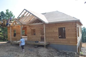 The log house with its roof sheathed and the front porch framing going up, the crew working along the porch roof.