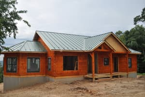 The finished metal roof over stained log walls, most windows set and one wide opening still empty, with a raw dirt yard in front.