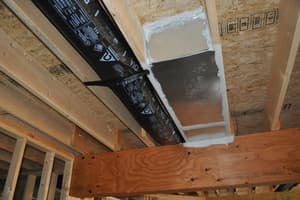 Looking up at floor framing where an insulated flexible duct feeds a foil-taped ceiling register boot beside a laminated beam.