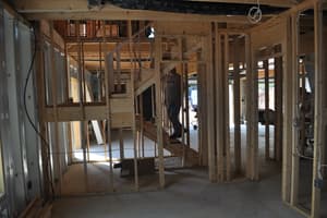 The lower level under framing, stud partitions and a rough stair in place on a poured concrete floor as a worker comes down the steps.