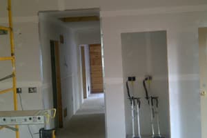 Drywall hung and taped through the main room and hallway, a rolling scaffold at left and a pair of drywall stilts standing in a closet opening.