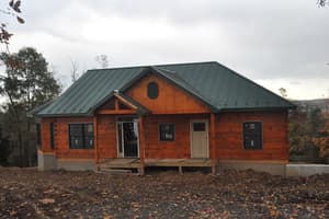 The finished exterior in late fall, stained log walls under a green metal roof, leaves down and the ground bare.