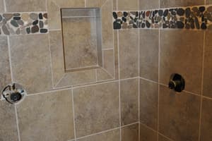 A tiled shower with a bench and an inset niche, a band of river stone across the wall.