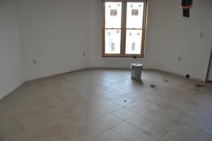 An empty room with painted walls, tile floor laid, and a window still carrying its factory stickers, one bucket left on the floor.