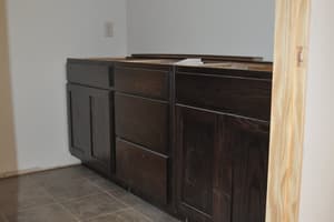 A room with painted walls and tile flooring where dark-stained base cabinets are set, a picture inlay worked into the tile floor.