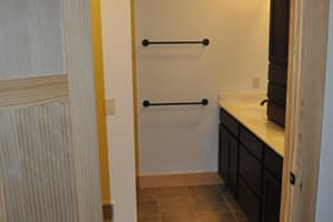 A paneled door standing open to a finished bathroom, a mosaic scene set into the tile floor, towel bars on the wall, and a dark vanity beyond.