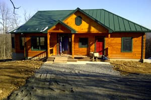 The finished front of a log home under a green standing-seam metal roof, with a gabled entry porch and a fresh gravel drive up to the steps.