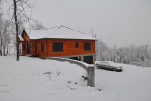 The home from the side in snow, its lower level walking out below a curving concrete retaining wall, with a snow-covered car parked beside it.