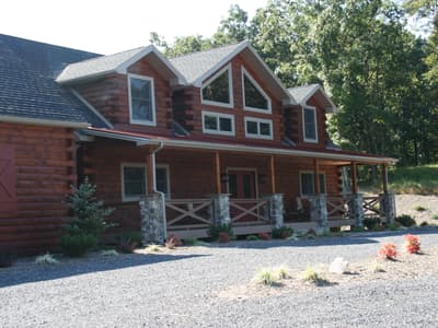 The front of a log home under a red porch roof, a prow gable of glass above the entry and rocking chairs on the porch