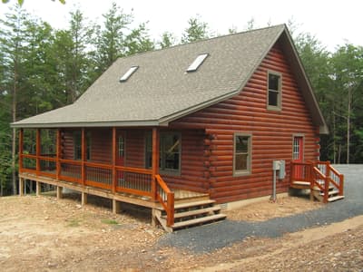 The home from the drive, porch posts and rail running the width of it under a low roof