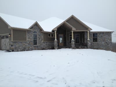 The finished house across snow, entry gable centered between the garage wing and the stone end