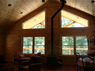 Two triangular gable windows above a wall of glass, the stove flue running up between them