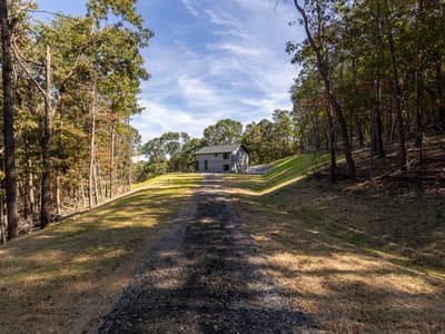 The home seen from far down the gravel drive, framed by woods on both sides of a mowed slope