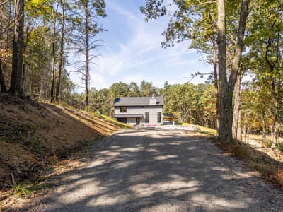 The home at the top of its gravel drive with flowers at the entries, seen from the tree-lined approach