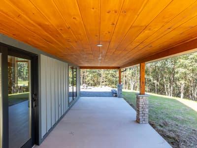 Covered patio with a pine plank ceiling, recessed lights, stone-clad pier columns and a sliding glass door into the house