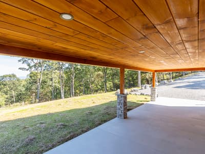 Corner of the covered patio looking past stone piers to the gravel drive and a hazy ridge on the horizon