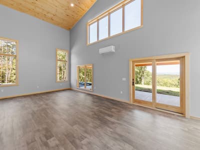 Empty great room corner with a clerestory window band, wall-mounted mini-split, and a sliding glass door to the patio and lawn
